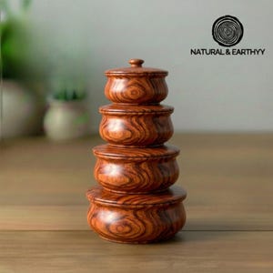 May include: A stack of four wooden bowls with lids, each a different size, showcasing a rich, reddish-brown wood grain pattern. The bowls are arranged from largest at the base to smallest at the top, creating a tiered effect. The logo "NATURAL & EARTHYY" is visible.