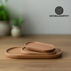 Puede incluir: Tres bandejas de madera ovaladas de diferentes tamaños apiladas sobre una superficie de madera. Las bandejas son de color marrón claro con un acabado liso. La bandeja más grande está en la parte inferior, con las bandejas mediana y pequeña anidadas encima. El texto "NATURAL & EARTHYY" está en la esquina superior derecha.