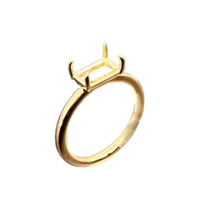 Puede incluir: Un anillo dorado con un engaste rectangular para una piedra preciosa. El anillo tiene una banda delgada y un engaste de cuatro garras, ideal para una joya personalizada.