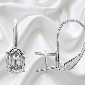 May include: A pair of silver-toned metal earring settings featuring an oval-shaped prong mounting for a gemstone. Each earring includes a secure lever-back closure mechanism, designed to hold a single stone in a vertical orientation for display.