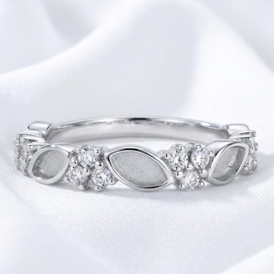 May include: A silver-toned ring featuring an alternating pattern of marquise-shaped metal segments with a matte finish and clusters of three small, round, clear, faceted stones set along the band in a continuous, symmetrical design.