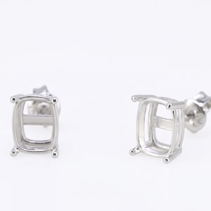 May include: Two silver-colored cushion-shaped earring settings. Each setting has four corner prongs and a post for securing the earring. The settings are designed to hold square or rectangular gemstones.