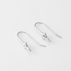 May include: A pair of silver-toned earring hooks featuring a curved, U-shaped wire design. Each hook terminates in a decorative, three-pronged metal element with a small circular loop at the base, intended for attaching jewellery components.
