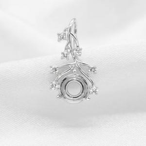 May include: A silver-toned pendant setting featuring a central circular mount for a gemstone, surrounded by delicate, branch-like metalwork adorned with six small, clear, round-cut stones arranged in a climbing, organic pattern.