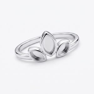 Könnte beinhalten: Ein silberner Ring mit einem blattartigen Design. Der Ring hat drei offene, oval geformte Fassungen, die Blättern ähneln und entlang des Rings angeordnet sind. Der Ring besteht aus glänzendem, reflektierendem Metall und ist vor einem weißen Hintergrund platziert.