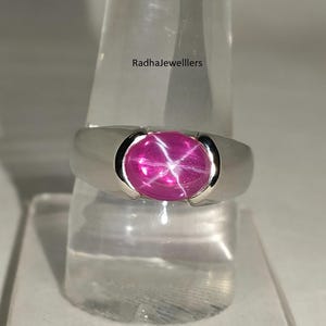 Peut inclure: Bague en argent ornée d'un grand rubis étoilé ovale. Le rubis est d'un rose vif avec un effet d'étoile à six rayons. La bague a un anneau lisse et poli et un sertissage à lunette qui maintient la pierre précieuse.