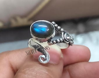 May include: A silver ring with a large, oval, iridescent labradorite stone. The ring has a unique, swirling design with decorative beaded accents and the text "SILVER HUB MS".
