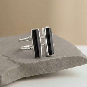 May include: A silver ring featuring two vertical black rectangular stones. The ring has a double band design and is set against a neutral background. The ring is a piece of jewelry.