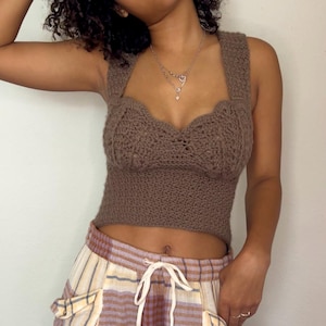 May include: A brown crochet top with a sweetheart neckline and wide straps. The top is paired with patterned pants featuring a mix of stripes and plaid in shades of purple, yellow, and cream. The pants have large pockets and a drawstring waist.