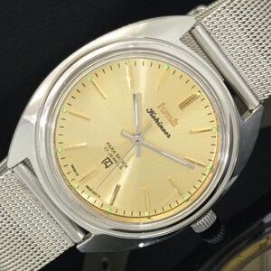 Peut inclure: Une montre vintage HMT Kohinoor avec un cadran doré et un bracelet en maille argentée. Le cadran de la montre présente des aiguilles et des marqueurs dorés, avec le texte "PARA SHOCK 17 JEWELS" et "MADE IN INDIA". La montre a un cadran rond et une lunette argentée.
