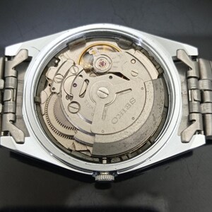 May include: A silver-toned wristwatch with an exposed mechanical movement visible through the open case back. The internal rotor is engraved with the word SEIKO and features visible gears, springs, and a balance wheel within the metallic housing.