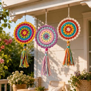 May include: Three circular crochet wall hangings featuring intricate mandala patterns in vibrant colours including yellow, pink, blue, and purple. Each piece is finished with a long, multi-coloured yarn tassel suspended from a central wooden bead.
