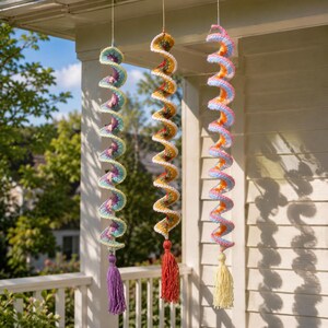 May include: Three spiral crochet decorations hanging from a porch. Each has a different colour scheme, including purple, yellow, orange, and blue. Each spiral ends with a tassel in a coordinating colour. These decorative items are suitable for indoor or outdoor use.