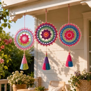 May include: Three circular crochet wall hangings featuring intricate, multi-colored floral patterns in shades of pink, blue, green, and purple. Each piece is suspended by a string and finished with a decorative yarn tassel at the bottom.