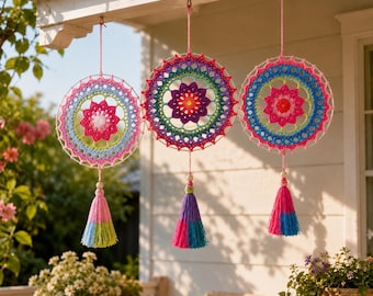 May include: Three circular crochet wall hangings featuring intricate, multi-colored floral patterns in shades of pink, blue, green, and purple. Each piece is suspended by a string and finished with a decorative yarn tassel at the bottom.