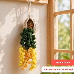 May include: A handmade crochet hanging planter with a cream-colored pot, filled with a brown interior and cascading green and yellow crocheted plant. The planter is suspended by a cream-colored cord. The text "BUY 1 GET 1" and "FRIENDLY PATTERN PDF" are visible.