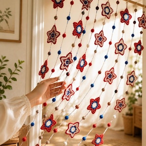 May include: Crocheted star curtain in red, white, and blue. The curtain features multiple star-shaped ornaments with a central white star, interspersed with red, blue, and beige beads. The curtain is hanging in a doorway.