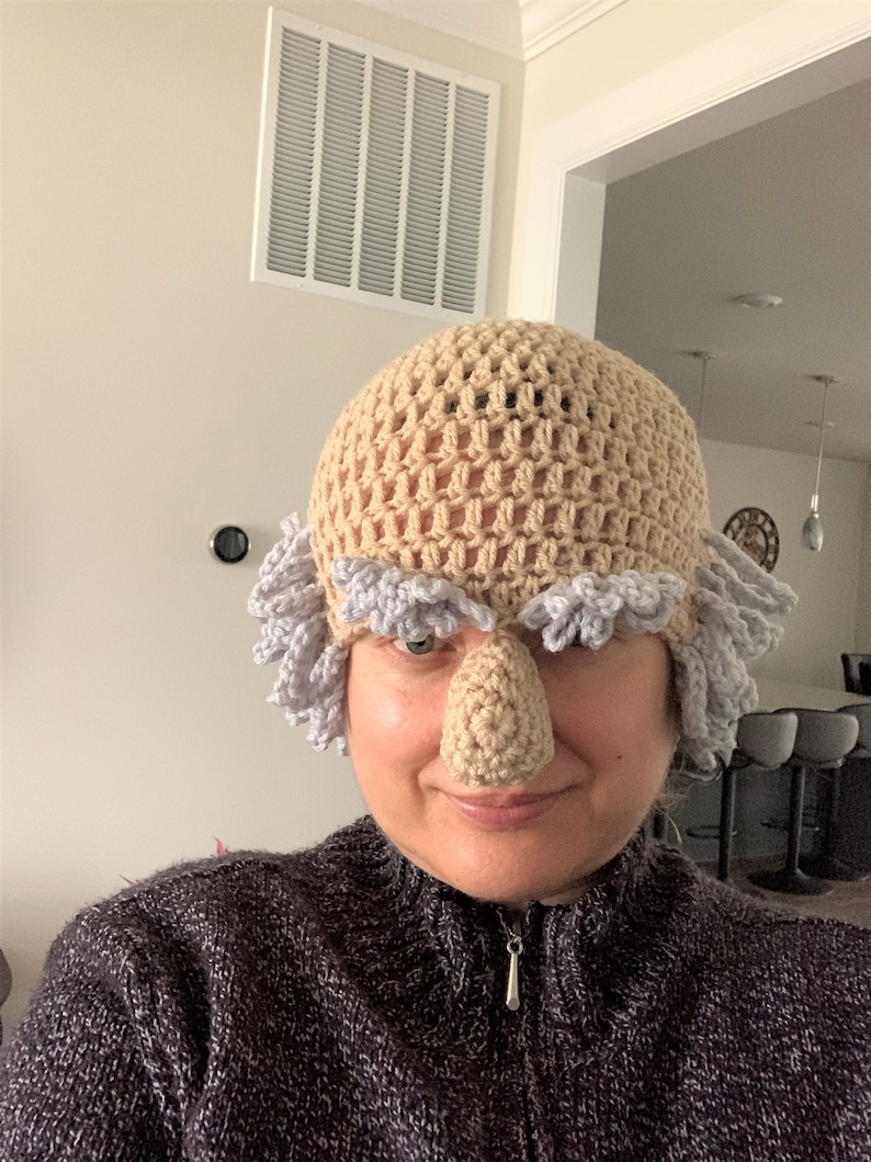 May include: A crocheted hat with a large, brown nose and gray hair. The hat is worn by a person with a gray sweater.