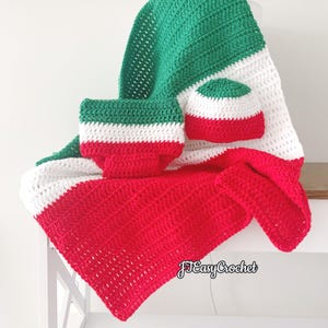 Puede incluir: Juego de bebé de ganchillo hecho a mano, que incluye una manta, un gorro y una braguita, en rojo, blanco y verde. La manta está doblada y colocada sobre una superficie blanca, con el gorro y la braguita encima.