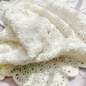 May include: Cream-colored, handmade crochet blanket with a textured stitch pattern. The blanket is folded, revealing the intricate details of the yarn and the scalloped edge. The blanket is soft and inviting, perfect for adding warmth and style to any space. The text "JTEasyCrochet" is visible.