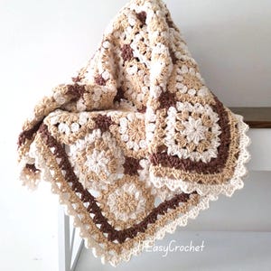 May include: A handmade crochet blanket featuring a repeating granny square pattern in shades of cream, beige, and dark brown. The blanket has a scalloped edge border and includes the text EasyCrochet printed in white in the bottom right corner.
