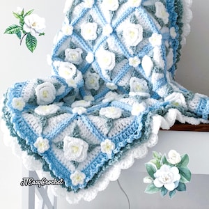 Beautiful crochet granny square blanket is hanging from a display on a light grey background. Each white granny square has a white textured gardenia flower in the center, framed with pale green leaves and light frosty blue border, so the whole blanket remind of a frozen gardenia blanket. There are also bunches of gardenia flowers in the image to highlight the likeness. The lettering logo says: " JTEasyCrochet"