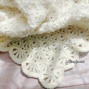 May include: Cream-colored crochet blanket with a scalloped edge. The blanket is folded, revealing the intricate stitch pattern and texture. The text "JTEasyCrochet" is visible on the edge of the blanket.