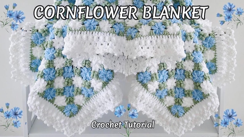 May include: A crocheted blanket with a floral design. The blanket has a repeating pattern of blue and white flowers with green details, and a white, ruffled edge. The text "Cornflower Blanket" and "Crochet Tutorial" are displayed.
