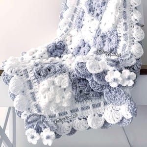 May include: A handmade crochet blanket in shades of white and light blue. The blanket features a floral design with square and scalloped edges. The text "JJEasy Crochet" is visible on the blanket.