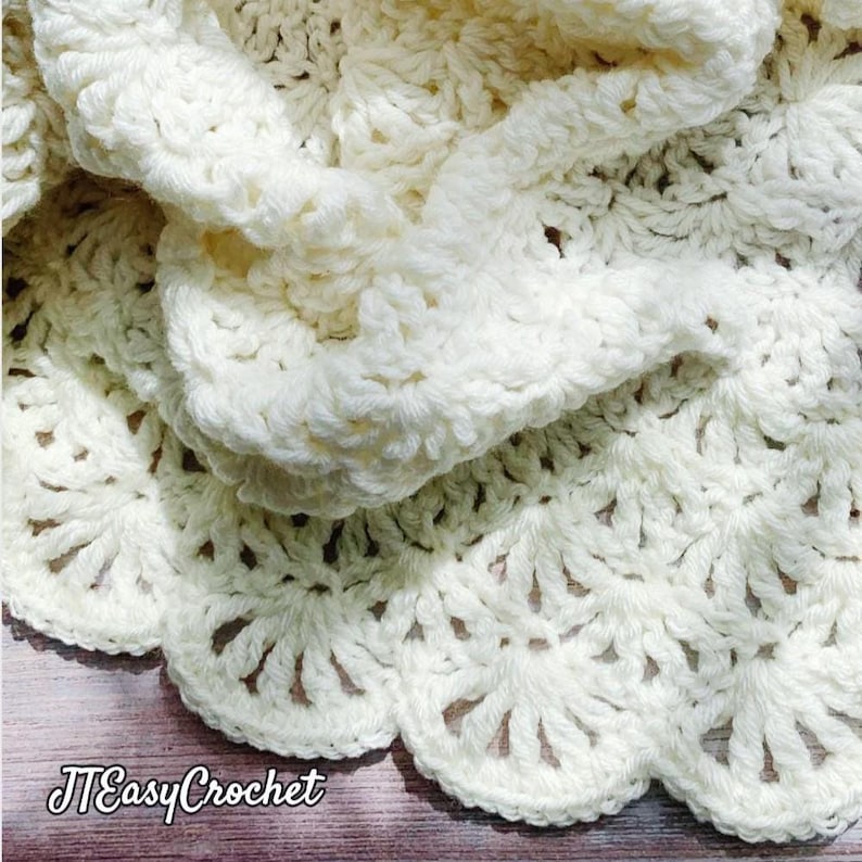 May include: Cream-colored, handmade crochet blanket with a scalloped edge. The blanket features a detailed, textured stitch pattern. The text "JTEasyCrochet" is visible in the lower left corner. The blanket is folded, showing the intricate design.