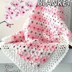 May include: A handmade crochet flower blanket in white and pink, with a floral pattern. The blanket features a white border and the text "CROCHET FLOWER BLANKET". The image also includes the text "Fun Crochet Ideas by JTEasyCrochet" and "Easy Crochet Pattern".