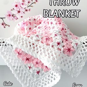 May include: A handmade crochet throw blanket with a cherry blossom design. The blanket features white and pink yarn, with cherry blossom accents. The text "CHERRY BLOSSOM THROW BLANKET" is at the top of the image, with additional text at the bottom.