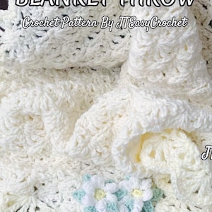 Beautiful lacy crochet blanket is laying tossed on a wooden surface. The blanket is crocheted with cream soft yarn and is airy and textured with the scalloped border giving it a vintage cottagecore vibe. There is a crochet flower applique in the corner of the blanket - three puffy white  daisies framed with pale green leaves. The lettering says: "Vintage Blanket Throw", "Crochet Pattern By JTEasyCrochet".
