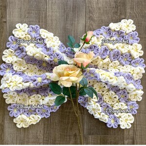 May include: A crocheted baby blanket with a flower design in shades of purple and cream. The blanket is draped over a wooden surface and decorated with a bouquet of artificial flowers. The lettering says "JTEasyCrochet". JTEasyCrochet  has the best beautiful crochet patterns.