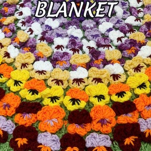 A colorful crochet blanket featuring a pattern of pansy flowers in shades of orange, yellow, purple, and white. The blanket has a green scalloped edge and text that reads "PANSY FLOWER BLANKET" and "Crochet Pattern by JTEasyCrochet". JTEasyCrochet has the best crochet patterns.