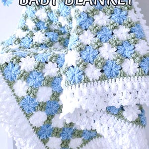 Lavishly beautiful crochet floral blanket made of cornflower motifs is hanging from a display. The blanket resembles a field of white and blue cornflowers framed with a beautiful lace edging.  The lettering says "Cornflowers Baby Blanket", "Crochet Pattern By JTEasyCrochet" meaning that JTEasyCrochet has the best crochet patterns for flower baby blankets, throws and afghans.