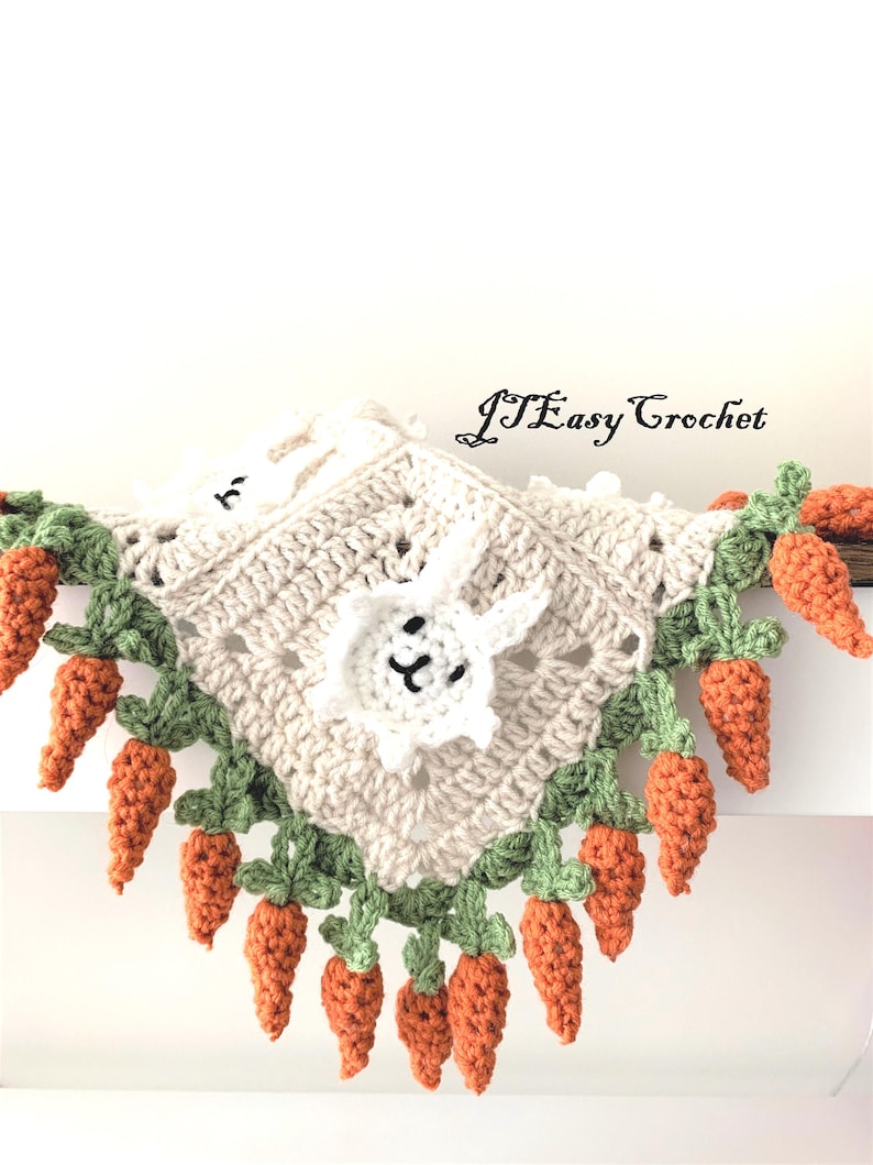 Puede incluir: Una manta de beb&eacute; tejida a crochet con un conejito blanco en el centro y un borde de hojas verdes y zanahorias naranjas. La manta est&aacute; hecha con hilo blanco y tiene un patr&oacute;n delicado y de encaje.