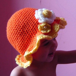 May include: A crocheted hat with a yellow and orange brim and a white flower with a pearl center.