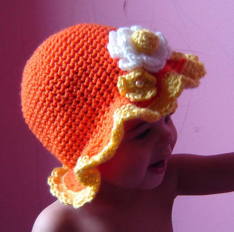 May include: A crocheted hat with a yellow and orange brim and a white flower with a pearl center.