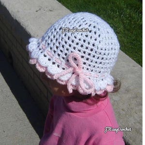 May include: White crochet hat with a pink bow and scalloped edge. The hat is worn by a child wearing a pink shirt. The text "JJEasyCrochet" appears twice in the image.
