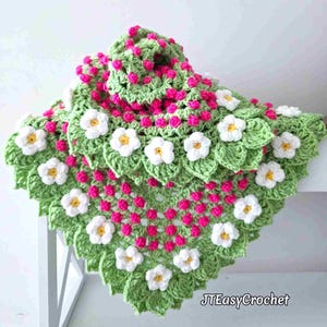 May include: A triangular crochet shawl featuring a light green base with a repeating pattern of small, vibrant pink bobble stitches and white five-petaled flowers with yellow centers. The text JTEasyCrochet is visible in the bottom right corner.