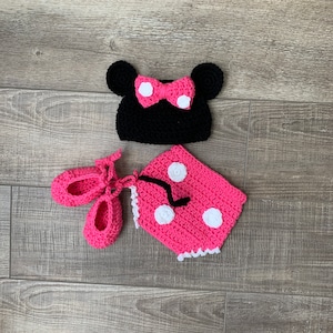 May include: A pink and black crocheted baby outfit with white polka dots. The outfit includes a hat, a dress, and shoes.