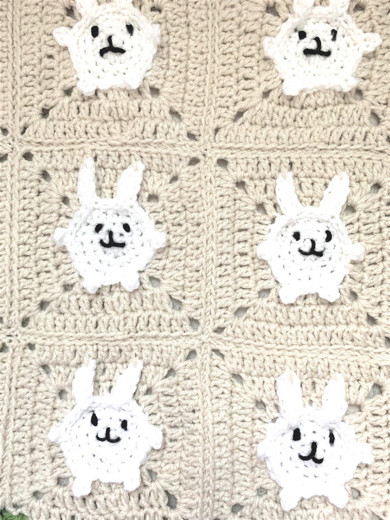 Puede incluir: Una manta de beb&eacute; de ganchillo con fondo beige y aplicaciones de animales de ganchillo blanco. Las aplicaciones tienen forma de corderos con ojos y narices negros.
