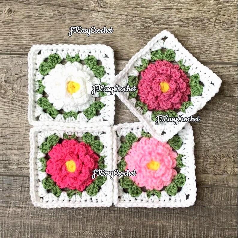 Set of four colorful 3D granny squares with raised borders laying on a flat surface. Each granny square has a white or shades of pink rose or peony with 2 layers of petals surrounded with green leaves.