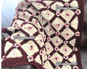 May include: A crocheted throw blanket with a burgundy and cream color scheme. The blanket features a repeating pattern of squares with 3D flower accents. The text "JJ Easy Crochet" is visible in the image.