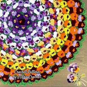 May include: A colorful, crocheted circular rug or doily featuring a floral pattern. The design incorporates various shades of purple, white, yellow, and orange, with a green scalloped border. The text "Crochet Pattern by JTEasyCrochet" is visible.