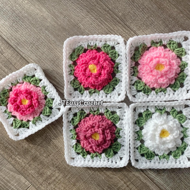 Set of five 3D white granny squares with raised borders laying on a flat surface. Each granny square has a white or shades of pink rose or peony with 2 layers of petals surrounded with green leaves.