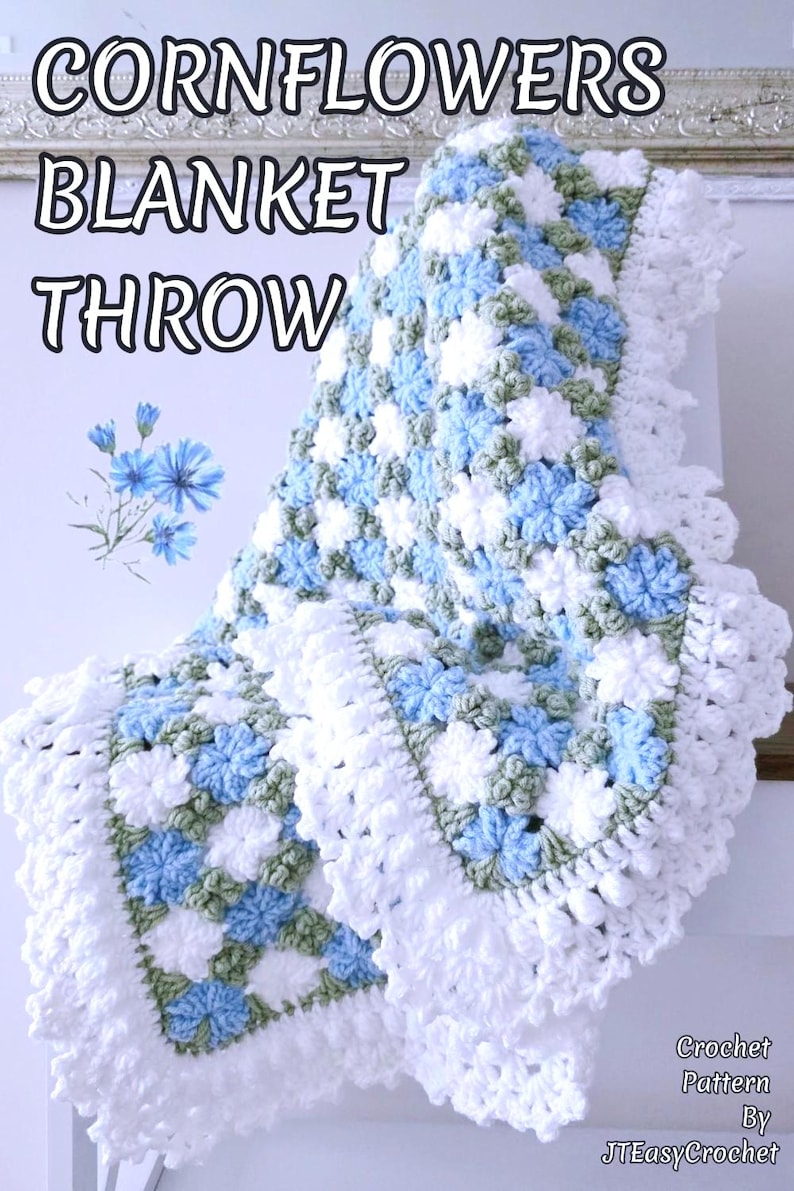Lavishly beautiful crochet floral blanket made of cornflower motifs is hanging from a display. The blanket resembles a field of white and blue cornflowers framed with a beautiful lace edging.  The lettering says "Cornflowers Blanket Throw", "Crochet Pattern By JTEasyCrochet" meaning that JTEasyCrochet has the best crochet patterns for flower baby blankets, throws and afghans.