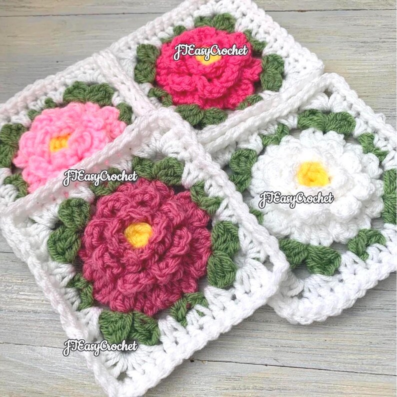 Set of four 3D white granny squares with raised borders laying on a flat surface. Each granny square has a white or shades of pink rose or peony with 2 layers of petals surrounded with green leaves.