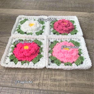 Set of four 3D white granny squares with raised borders laying on a flat surface with angled perspective. Each granny square has a white or shades of pink rose or peony with 2 layers of petals surrounded with green leaves.